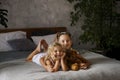 Two little sisters in white dresses laying at bed at daylight with bear toy. Family unity concept. Royalty Free Stock Photo