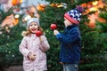 Two little smiling kids, boy and girl eating crystalized sugared apple on German Christmas market. Happy friends in Royalty Free Stock Photo