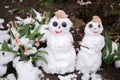 Two little smiling snowmen stand on a flowerbed with blooming early spring tulips Royalty Free Stock Photo