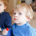 Two little toddler boys, cute brother children watching cartoons on tv and eating lolipop candy. Happy siblings together