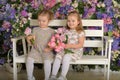 Little twin girls in the garden on a bench against the background of a floral wall with bouquets of flowers in their hands Royalty Free Stock Photo