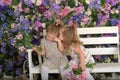 Little twin girls in the garden on a bench against the background of a floral wall with bouquets of flowers in their hands Royalty Free Stock Photo