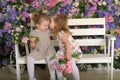 Little twin girls in the garden on a bench against the background of a floral wall with bouquets of flowers in their hands Royalty Free Stock Photo