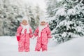 Two little twin girls in red suits stand in a snowy winter forest