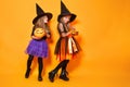 Two little witches in halloween costumes on orange background Royalty Free Stock Photo