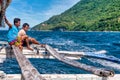 Two local banca crew members ride on an outrigger while motoring along Mindoro Island in the Philippines.