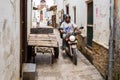 Two local men driving a motorcycle through narrow streets of Stone Town, old colonial center of Zanzibar City, Unguja, Tanzania.