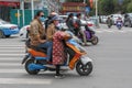 Two local Tibetan women wearing face masks and glasses riding a motorbike in Lhasa traffic standing on pedestrian wal