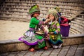 Two local Vietnamese kids in colorful traditional himalayan sherpa clothing dresses. Sister giving a drink to her younger sibling