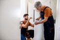 Two locksmith, repairmen, workers in uniform installing, working with house door lock using screwdriver. Repair, door Royalty Free Stock Photo