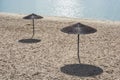 Two lonely reed umbrellas on an empty beach at noon under the sun