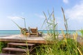 Two lounge chairs on wooden pier through grass. Empty tropical resort. Pair of deck chairs with pillows on tropical beach. Royalty Free Stock Photo