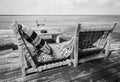 Two lounge chairs on wooden pier, monochrome. Empty tropical resort. Pair of deck chairs with pillows on beach, black and white. Royalty Free Stock Photo