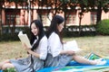 Two lovely Asian Chinese pretty girls wear student suit in school best friends smile laugh reading book sit on grass Royalty Free Stock Photo