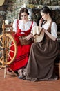 Two Lovely Caucasian Ladies Posing With Spinning Wheel And Fancywork Hoop in Retro Dress In Rural Environment