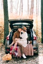 Two lovers embrace each other sitting in the trunk of a car, comfortably covered with blankets in a pine forest in the autumn