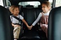 Two loving siblings sitting on a back seat of a car, holding hands