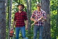 Two lumberjacks with chainsaw and axe. Male lumberjack in the forest. Woodcutter with axe and lumberjack with chainsaw.