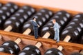 Two macro business figures standing on an abacus and discussing business