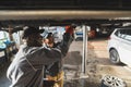 Two male auto mechanics replacing a clutch in a car on hydraulic lift in service shop