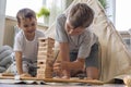 Two male children playing Jenga hardwood bricks tower construction childish room with linen wigwam