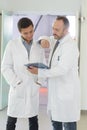 Two male doctors with clipboard at hospital corridor