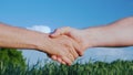 Two male farmers shake hands. Against the background of a green field and a blue sky. Deal in agribusiness concept Royalty Free Stock Photo