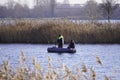 Two male fishermen in warm clothes on a boat, winter fishing on a river or lake. Photo through dry, brown reeds or grass