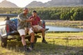 Two Male Friends With Backpacks In Pick Up Truck By Lake Drinking Beer Watching Sports On Phone Royalty Free Stock Photo