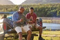 Two Male Friends With Backpacks In Pick Up Truck By Lake Drinking Beer Watching Sports On Phone Royalty Free Stock Photo