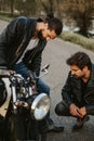 Two male friends looking seriously at motorcycle on the road