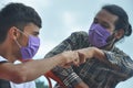 Two male friends wearing face mask with making fist bump in outdoor while looking each other Royalty Free Stock Photo