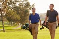 Two Male Golfers Walking Along Fairway Carrying Bags Royalty Free Stock Photo