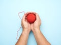Two male hands hold a ball of red woolen threads, blue background