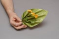 Two male hands hold a wavy decorative element and yellow flowers on a gray background