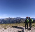 Two male hikers are pointing at the mountains far away and talking about what the names of those mountain are