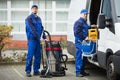 Two Male Janitor Unloading Cleaning Equipment From Vehicle