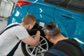 Quality with new standards. Two male mechanics using torch for inspecting wheel of lifted car at auto repair shop Royalty Free Stock Photo