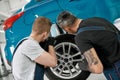 Service beyond standards. Two male mechanics using torch for inspecting wheel of lifted car at auto repair shop Royalty Free Stock Photo