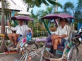 Two male pedicab drivers sit casually in their rickshaws waiting for the arrival of passengers