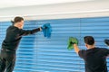 Two male professional cleaners cleaning blue blinds on a large window front with micro fiber cloths