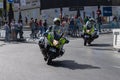 Male Spanish civil guards on motorcycles driving through a paved road with people in the background