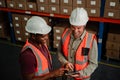 Two male workers scrolling on digital tablet discussing delivery process for parcels packaged in factory. Royalty Free Stock Photo