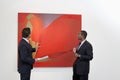 Two males talking over painting in art gallery