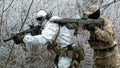 Two men in camouflage white, green uniform with machineguns. Soldiers with muchineguns go one after another in the winter forest. Royalty Free Stock Photo