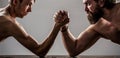 Two man`s hands clasped arm wrestling, strong and weak, unequal match. Heavily muscled bearded man arm wrestling a puny