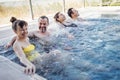 Two married couples chat and take an outdoor pool. Friends laugh and relax in the swirling water