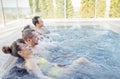 Two married couples chat and take an outdoor pool. Friends laugh and relax in the swirling water
