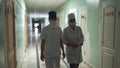 Two masked female nurses in white coats walking through hospital hall looking at camera. Hospital interior in process of