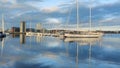 Two mast sailboat moored at a harbor under blue sky with coastal buildings in the background